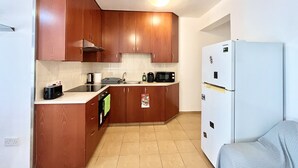 A compact kitchen with wooden cabinets, a built-in oven, a microwave, and a white refrigerator. - 38 AN - Stay Malanda Sun Apartment (Ayia Napa)