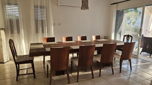 A dining area with a long wooden table and chairs, a window with blinds, and a door leading outside. - 126 PAP - Stay Villa Nefeli (Chlorakas)
