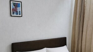 Ein ordentlich bezogenes Bett mit weißen Leinen in einem Zimmer mit schlichter Wand und einem gerahmten Bild.