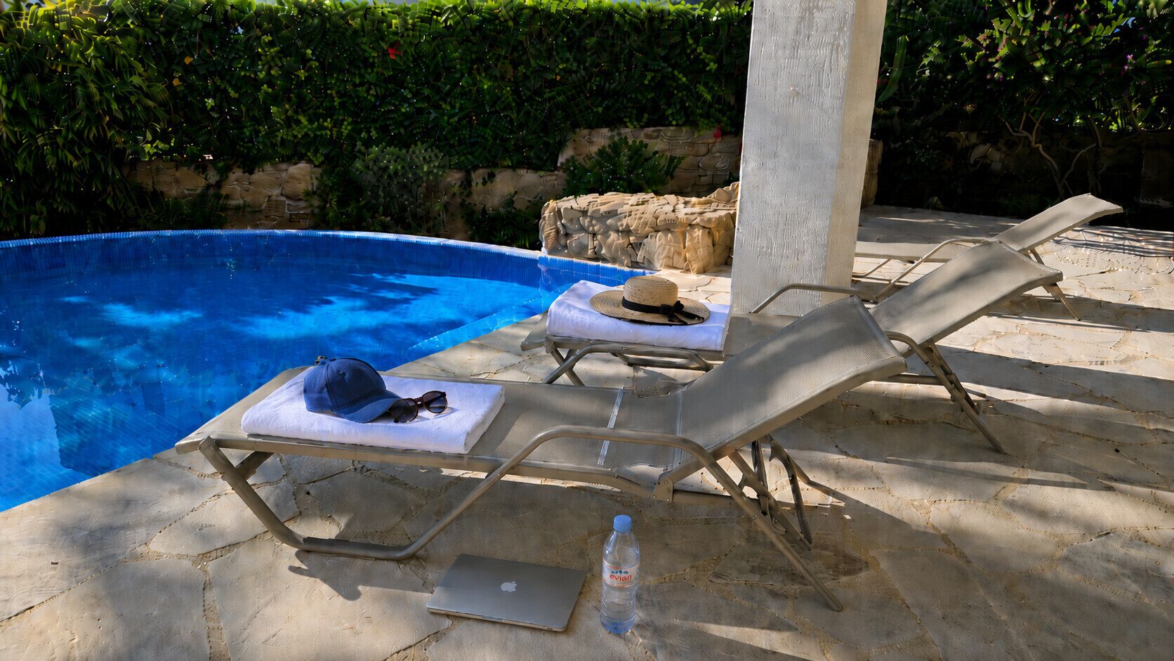 Ein Poolbereich mit Liegestühlen, einem Hut, Sonnenbrillen und einer Flasche.