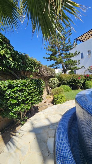 A stone pathway leading to a blue-tiled pool, surrounded by lush greenery and a white building. - 126 PAP - Stay Villa Nefeli (Chlorakas)