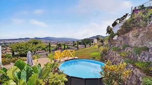 A swimming pool surrounded by lush greenery, with a view of a cityscape and mountains in the distance. - Casa de Limon (La Vega)