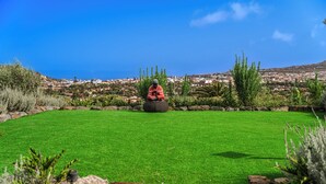 A well-maintained lawn with a statue in the center, surrounded by various plants and a stone pathway leading to a wooden bench. - Casa de Limon (La Vega)