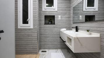 Un baño moderno con un tocador blanco, un grifo negro y suelo de mármol. Hay dos ventanas pequeñas con marcos blancos y un espejo sobre el tocador.