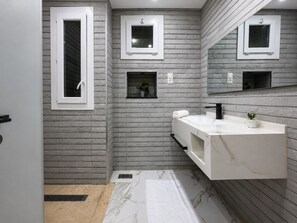 A modern bathroom with a white vanity, a black faucet, and a marble floor. There are two small windows with white frames and a mirror above the vanity. - Joli appartement 4 pièces à Constantine (El Khroub)