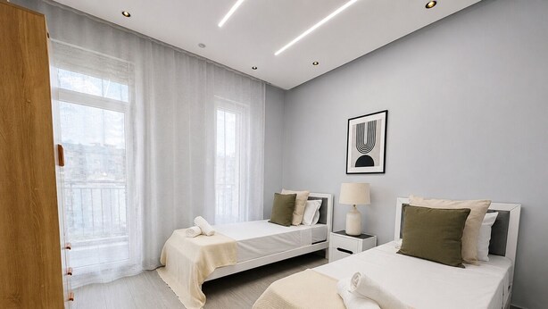 Habitación de hotel con dos camas, una mesita de noche, una lámpara y una ventana con cortinas.