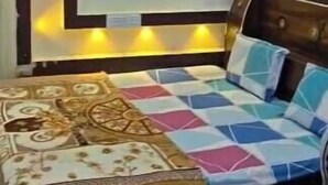 Un dormitorio con cama, cabecera y estante de pared con adornos.