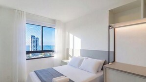 Ein Hotelzimmer mit einem Bett, einem Nachttisch, einem Spiegel und einem Fenster mit Blick auf Gebäude.