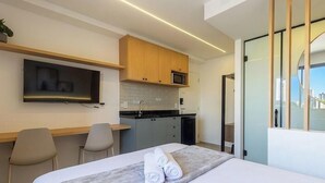 Ett modernt hotellrum med en säng, ett skrivbord, en platt-TV, en mikrovågsugn och utsikt över staden.