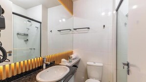 A modern bathroom with a glass shower enclosure, a white sink, and a toilet. - Studio in a Cond. With a gym in Downtown Muv0811 (Curitiba)