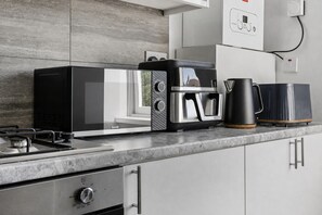 A modern kitchen with a gas stove, a coffee maker, a toaster, and a kettle on the countertop. - K Suites - Modern 4 bed Maisonette fits 9 (Beldevere)