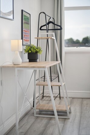 A modern workspace with a white desk, a black hanger, a potted plant, and a ladder. - K Suites - Modern 4 bed Maisonette fits 9 (Beldevere)
