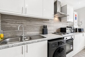 A modern kitchen with a stainless steel sink, a built-in dishwasher, and a stove. - K Suites - Modern 4 bed Maisonette fits 9 (Beldevere)