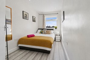Een slaapkamer met een bed, een raam, een radiator en een nachtkastje.