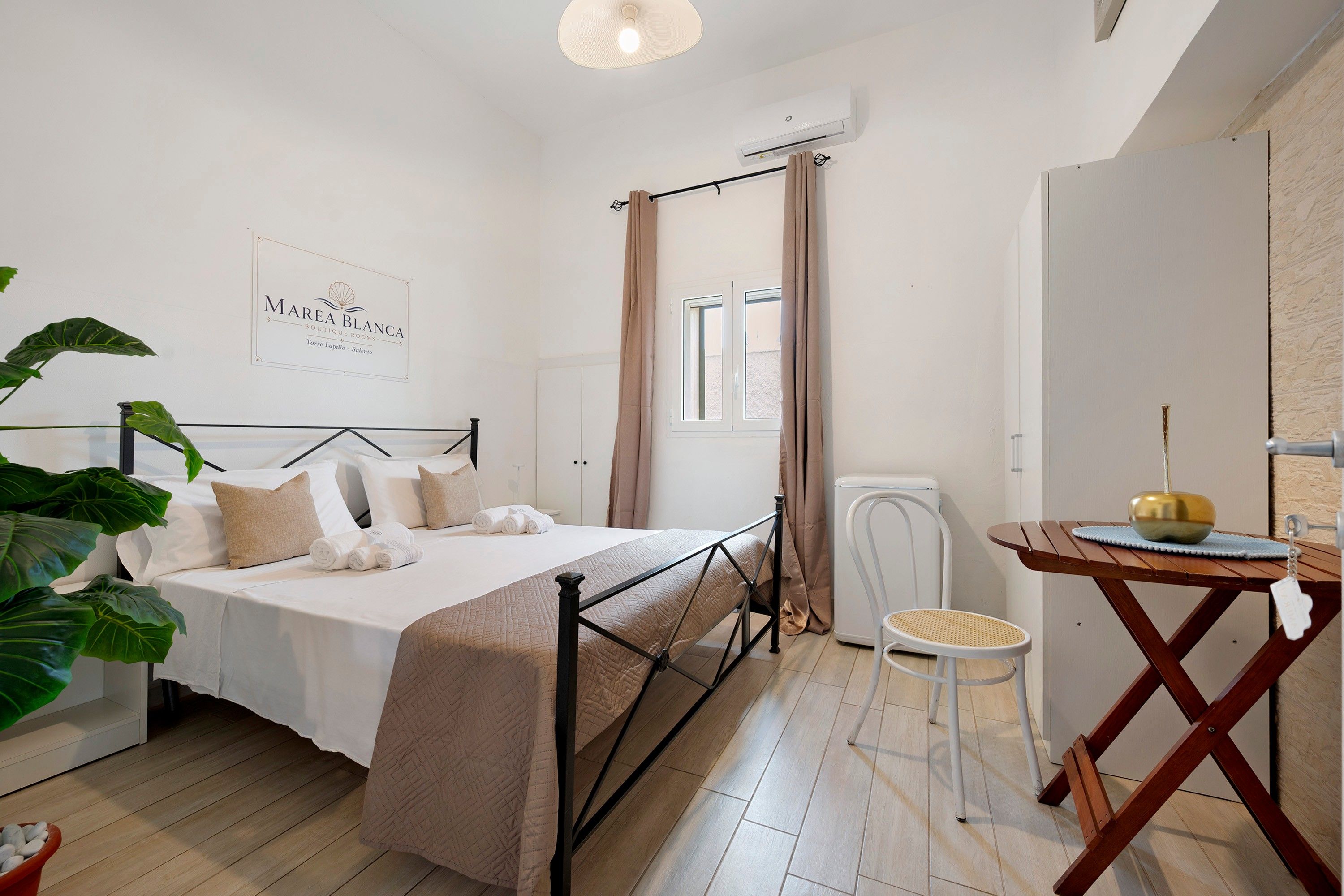 Une chambre à coucher comprenant un lit, un bureau, une chaise, une plante en pot et un climatiseur fixé au mur.
