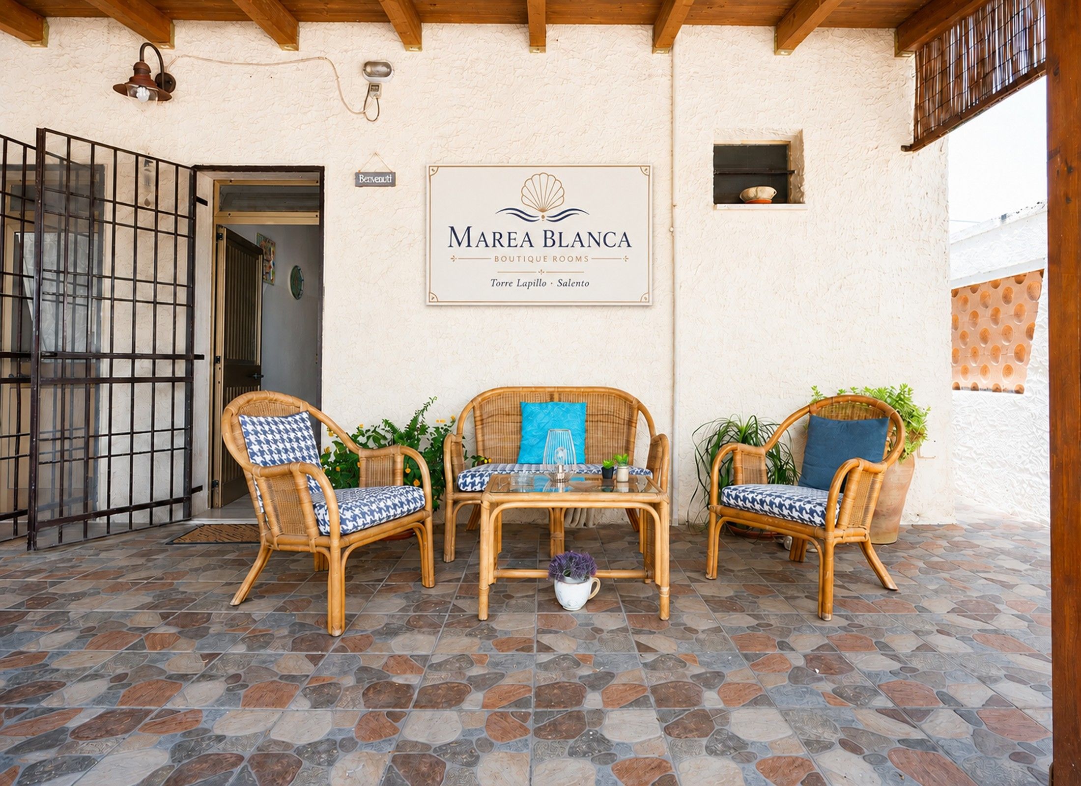 A patio with wicker furniture, a tiled floor, and a sign for 'Marea Blanca Boutique Rooms.'