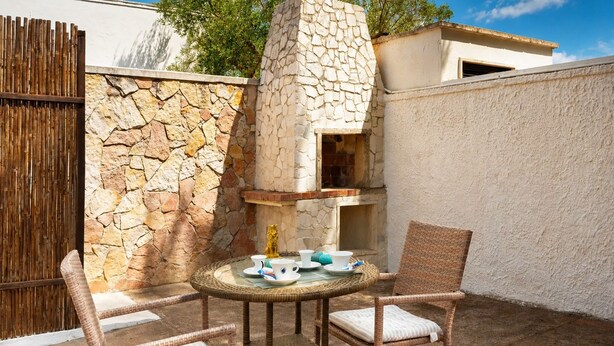 Une terrasse extérieure avec un four en pierre, des chaises en osier et une table préparée pour le thé.