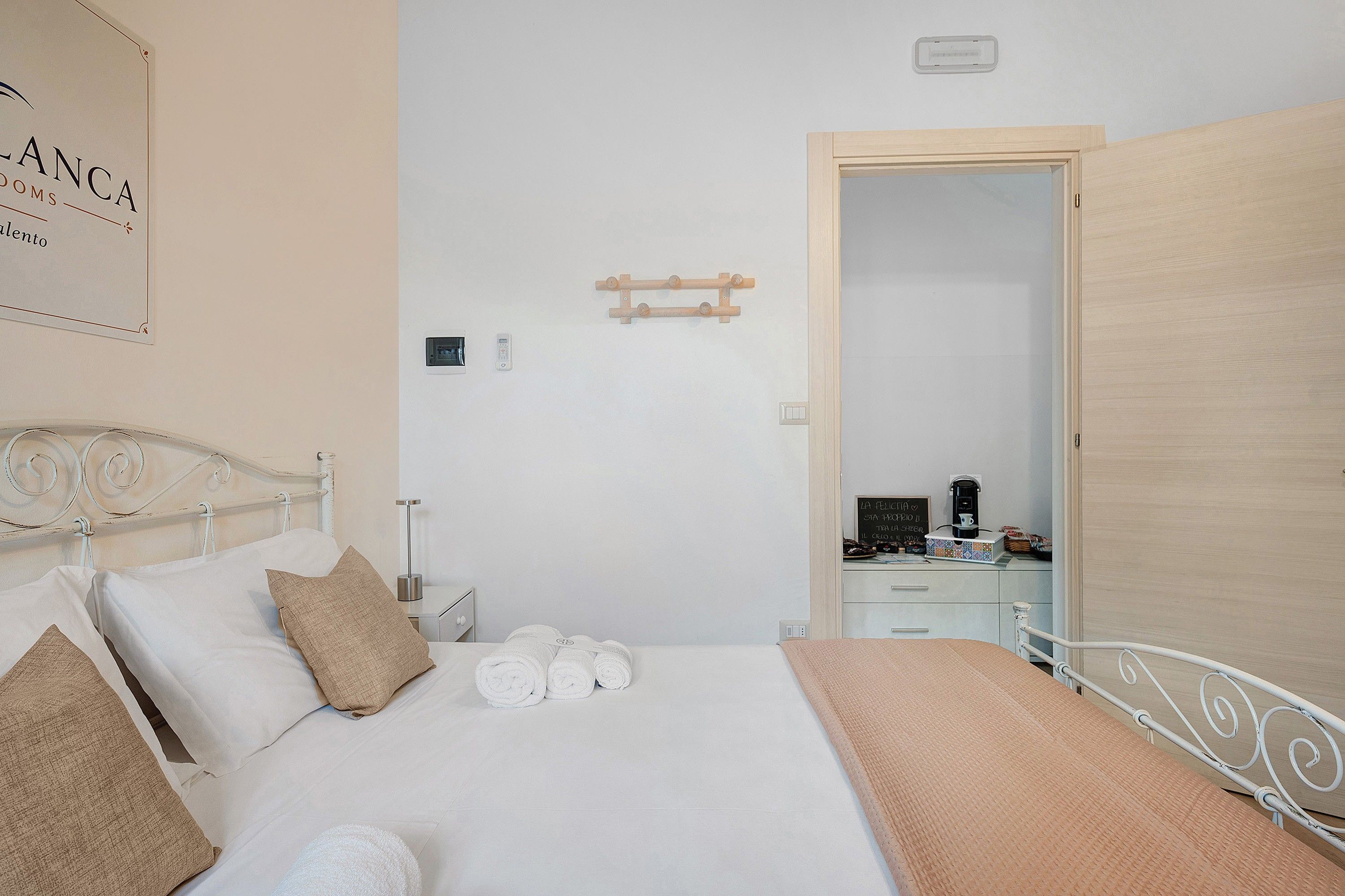 Una camera d'albergo con un letto, un comodino, una lampada a parete, una porta e un cartello al muro.