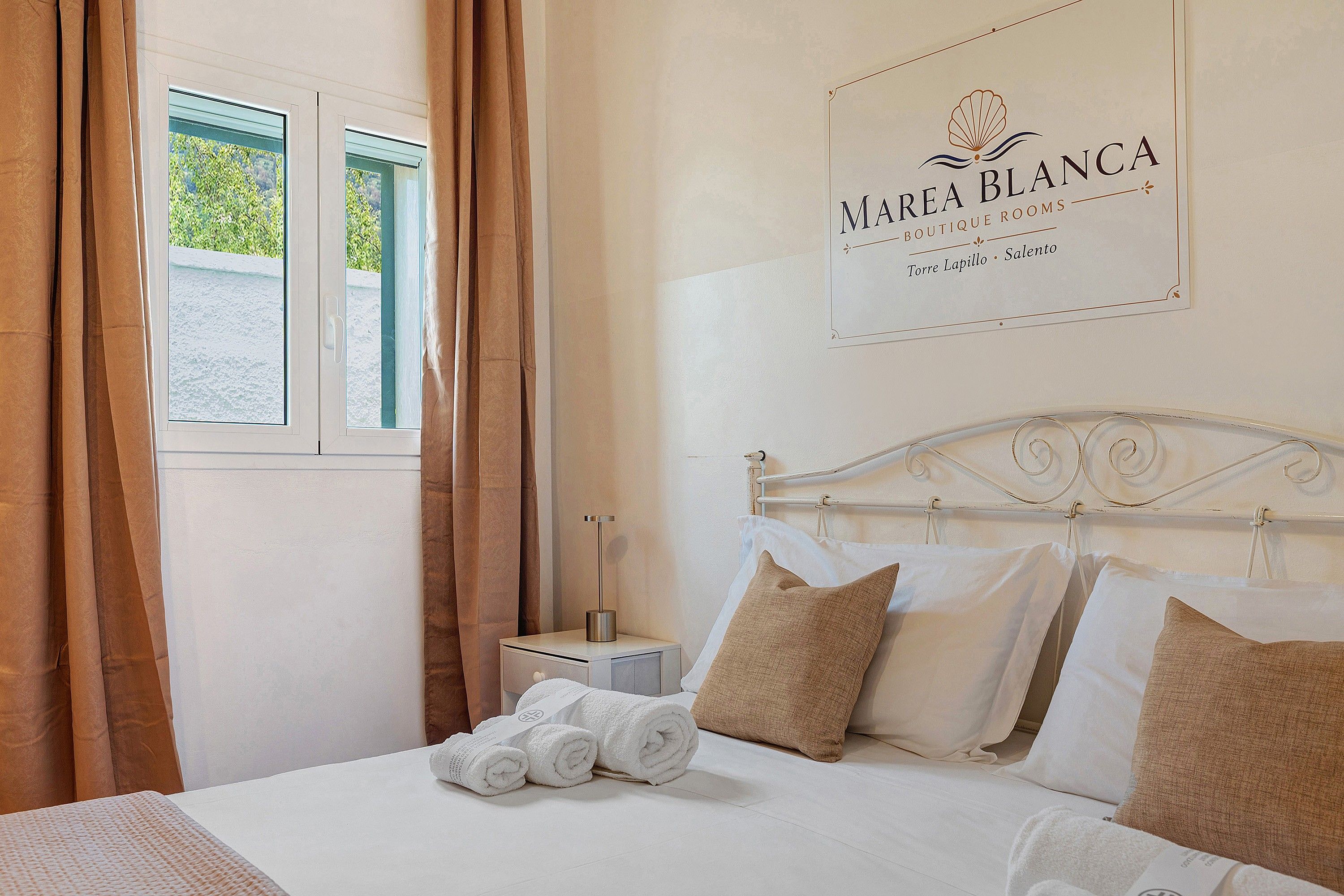 Una habitación de hotel con cama, almohadas, una mesita de noche y una ventana con cortinas.