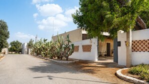 Une rue résidentielle bordée de cactus, un bâtiment blanc avec un mur beige et un ciel dégagé.