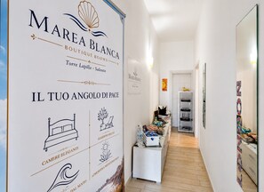 Un couloir d’hôtel avec une enseigne indiquant « Marea Blanca Boutique Rooms », une illustration représentant un lit et une étagère contenant divers objets.