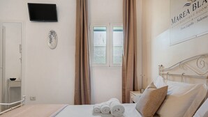 Une chambre d’hôtel équipée d’un lit, d’un téléviseur à écran plat, d’une fenêtre avec des rideaux et d’un panneau fixé au mur.