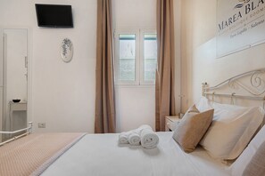 Habitación de hotel con cama, televisor de pantalla plana, ventana con cortinas y un cartel en la pared.