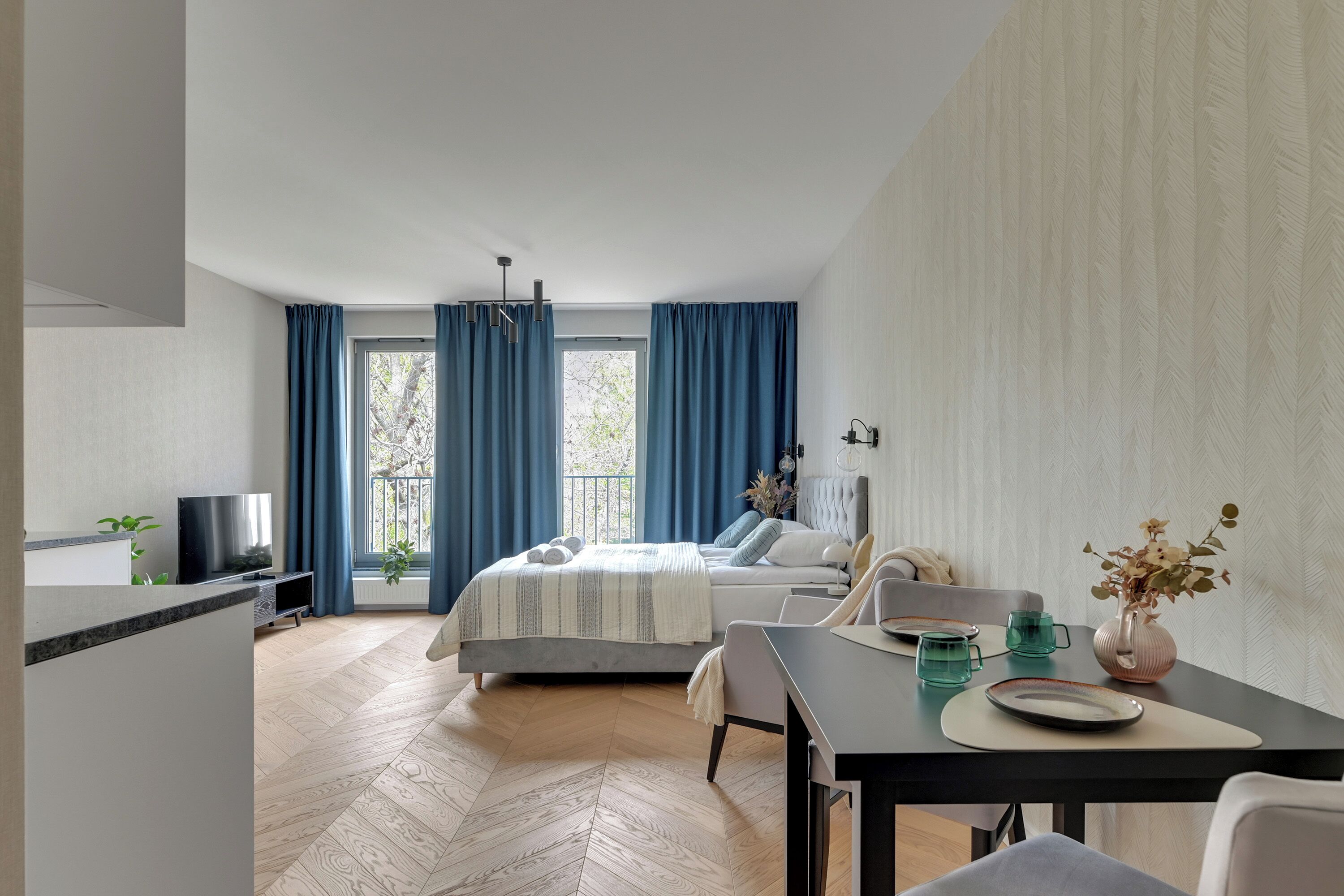 A modern hotel room with a bed, a dining table, and a TV.