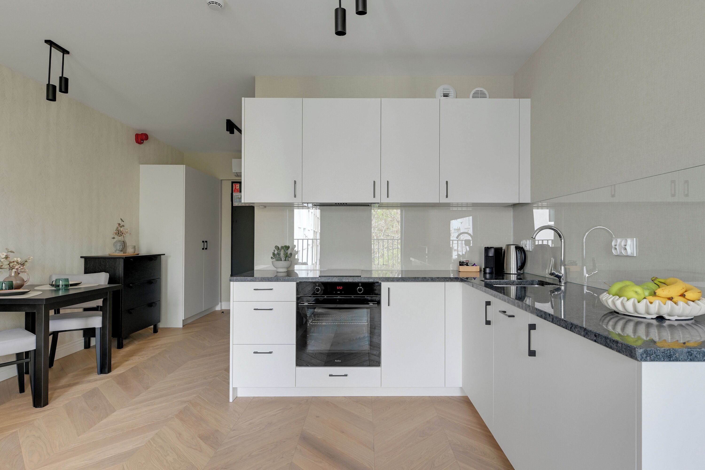 Eine moderne Küche mit weißen Schränken, einem eingebauten Backofen und einer Obstschale auf der Arbeitsplatte.