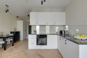 A modern kitchen with white cabinetry, a built-in oven, and a fruit bowl on the counter. - Sukiennicza by BrowarHeveliusApartments (Gdańsk)