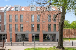 A modern brick building with multiple windows and a tree in the foreground.