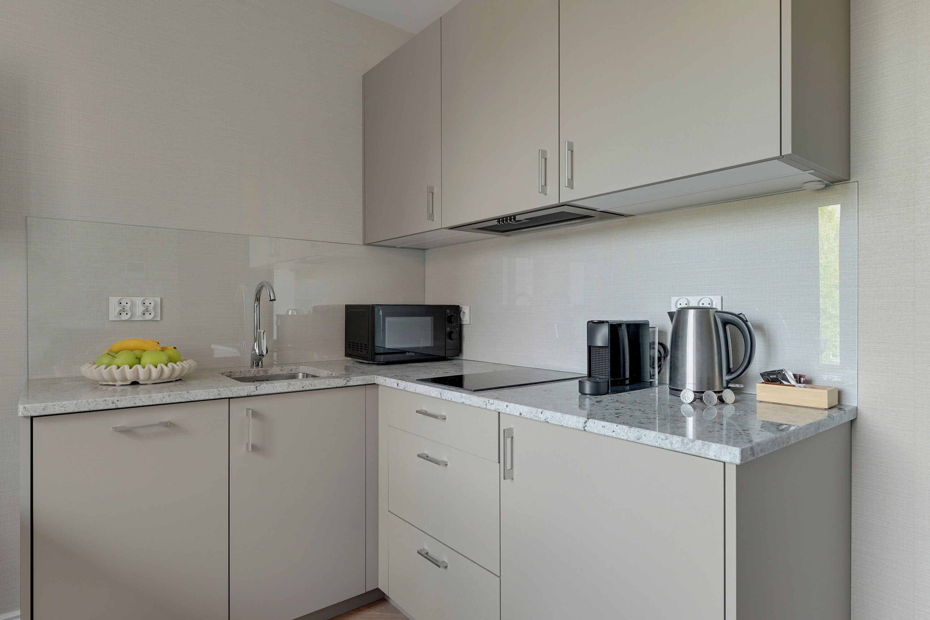 Una cucina compatta con forno a microonde, bollitore e una ciotola di frutta sul piano di lavoro.