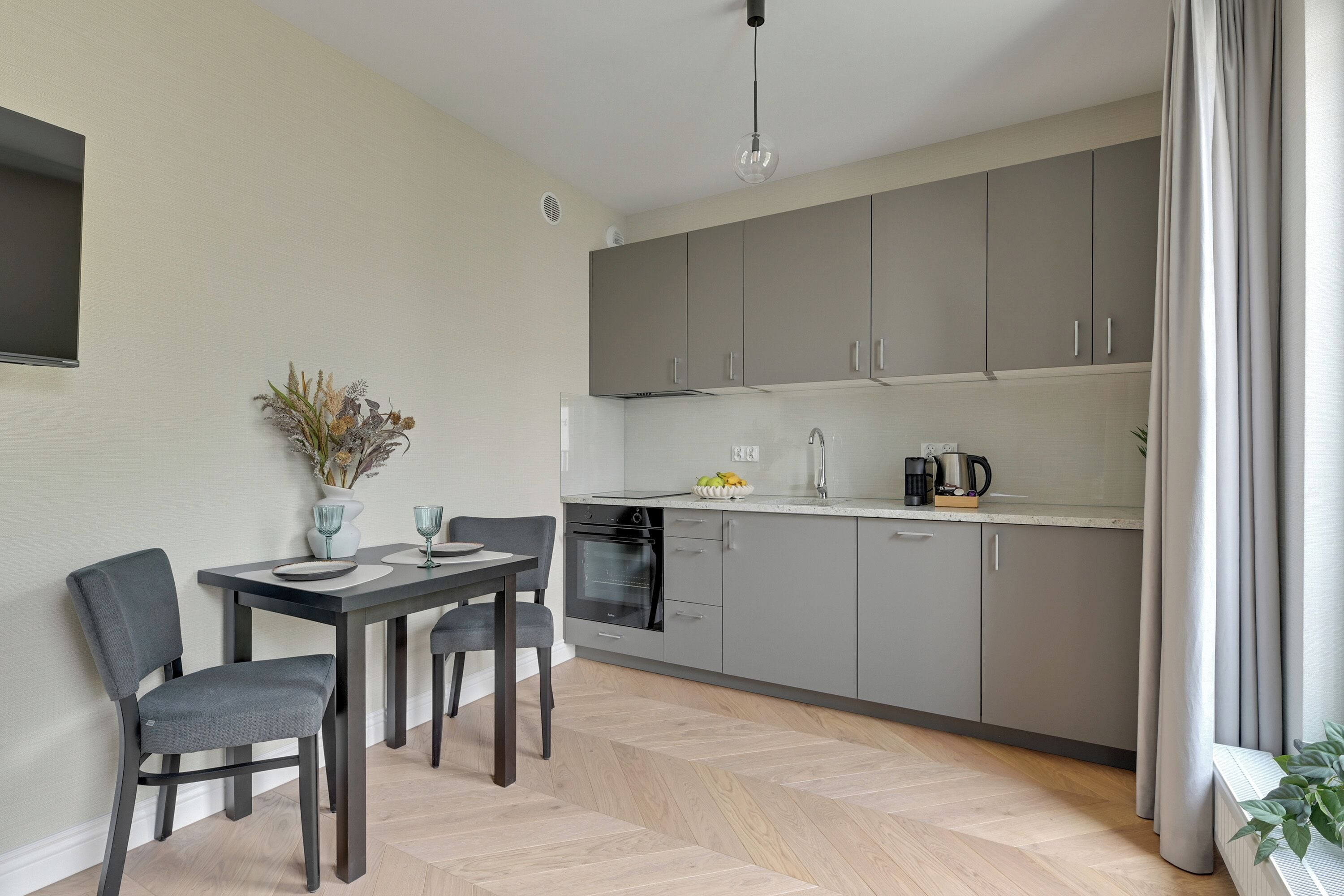 Une cuisine moderne avec des meubles de couleur grise, une table à manger avec des chaises et un luminaire suspendu.