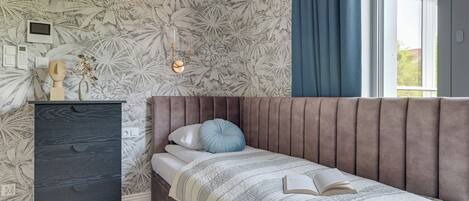 A bedroom with a bed, a dresser, a wall-mounted light, and a window with curtains.