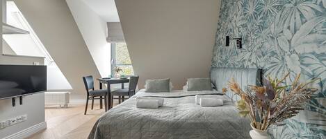 A modern bedroom with a large bed, a TV, a dining area, and a window with a view.