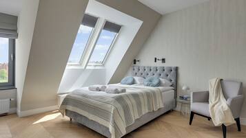 Un dormitorio con techo inclinado, una cama con cabecera capitonada, una silla y una ventana con persianas.