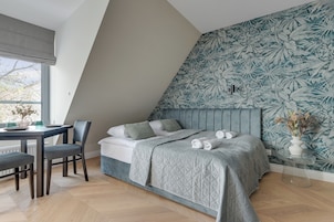 A bedroom with a sloped ceiling, a bed with a quilted bedspread, a desk with a chair, and a window with a view of trees.