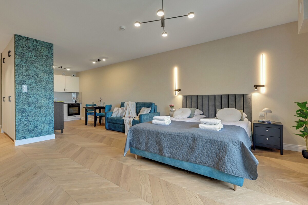 A modern hotel room with a large bed, a desk, and a kitchenette.