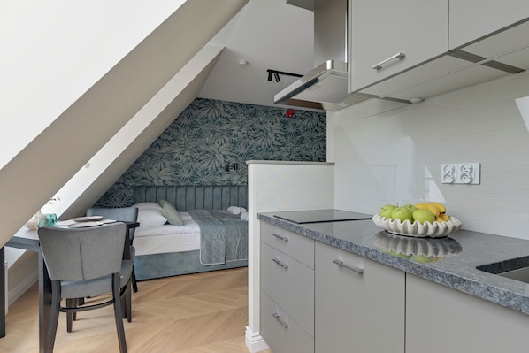 A modern kitchen with a built-in stove, a dining area with a table and chairs, and a bedroom with a bed and a nightstand.