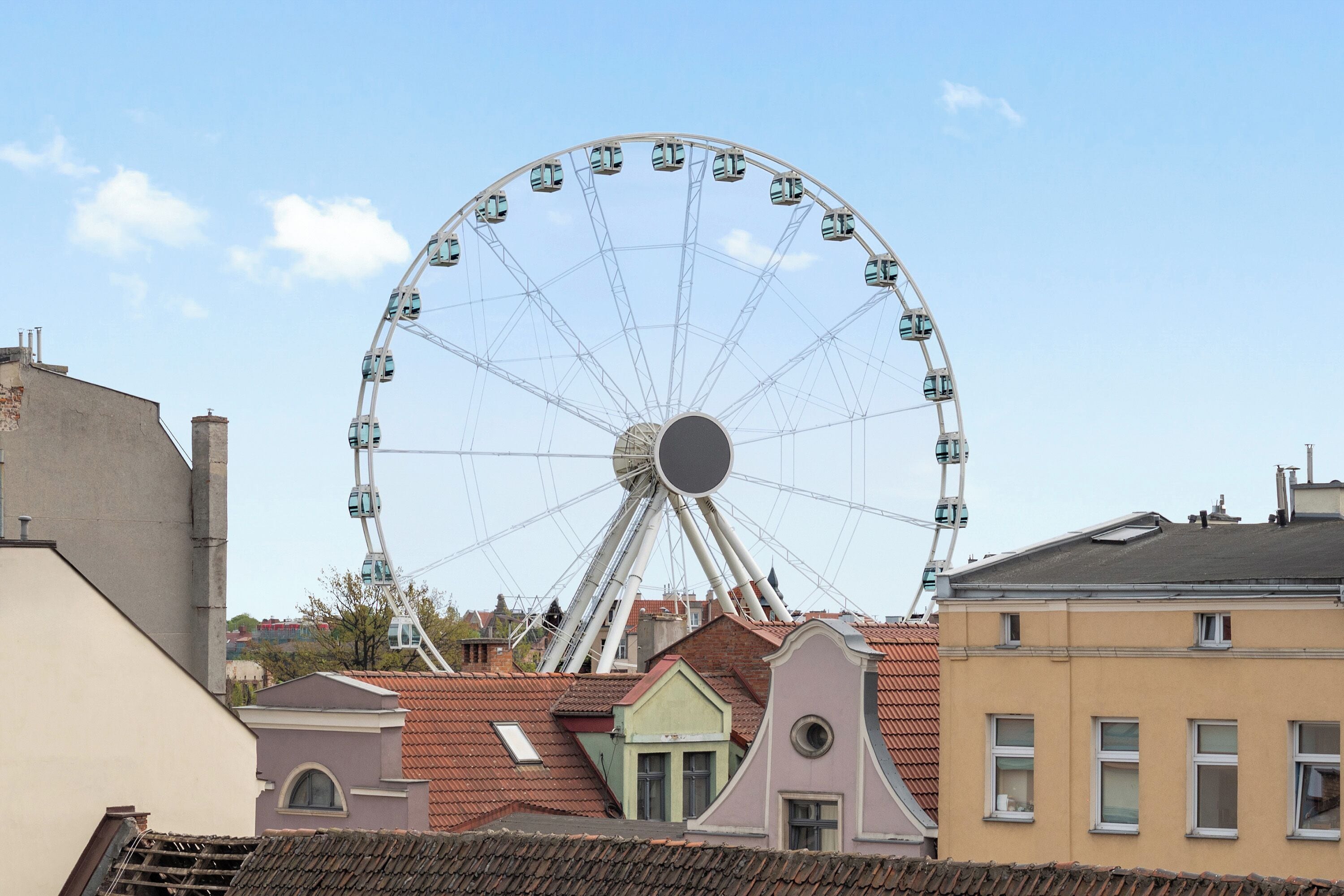 Ein Riesenrad mit Gondeln, umgeben von Gebäuden mit roten Ziegeldächern.