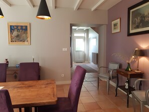 Uma área de refeições com uma mesa de madeira e cadeiras roxas, um corredor que leva a uma porta e uma luminária sobre uma mesa lateral.