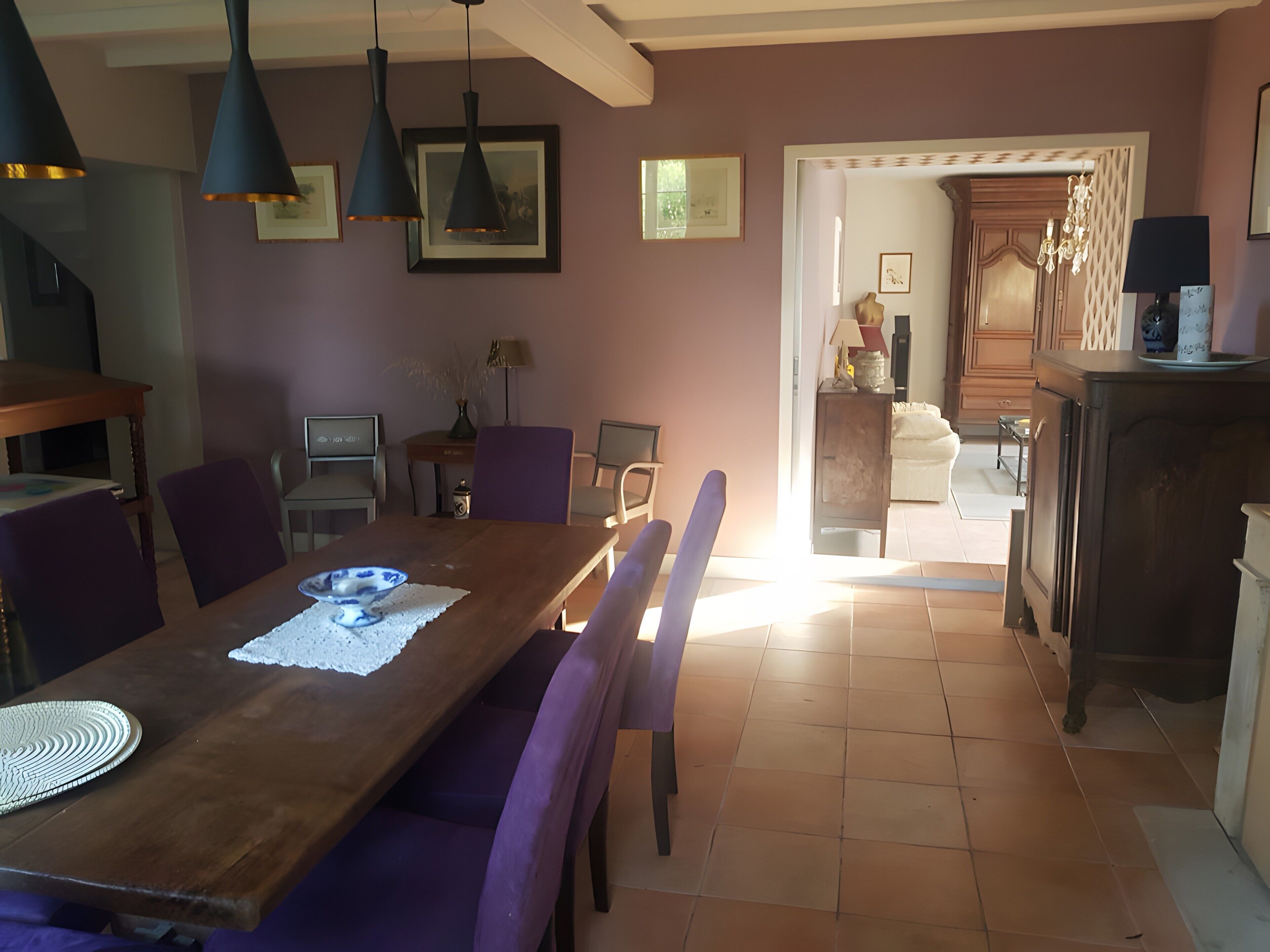 Ein Essbereich mit einem Holztisch, violetten Stühlen, Pendelleuchten und gerahmten Bildern an den Wänden.