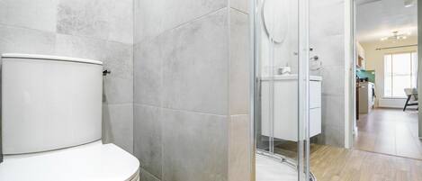 A modern bathroom with a toilet, shower, and glass-enclosed sink area.