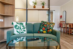 A living room with a sofa, a glass coffee table, a remote control, and a dining area with a chair and table. - Studio Sleeps 2 With Parking (Belfast)