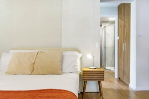 A bedroom with a bed, bedside table, and a shower area.