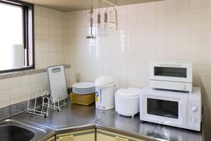 A kitchen with a stainless steel sink, a microwave, a rice cooker, and a stack of plates. - Sweetpad (Setagaya City)