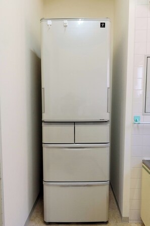A white refrigerator with a freezer on top and a bottom freezer, located in a corner of a room with white walls and a tiled floor. - Sweetpad (Setagaya City)