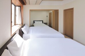 Une chambre d’hôtel avec deux lits, une fenêtre avec des rideaux, une porte et une vue sur une autre chambre.