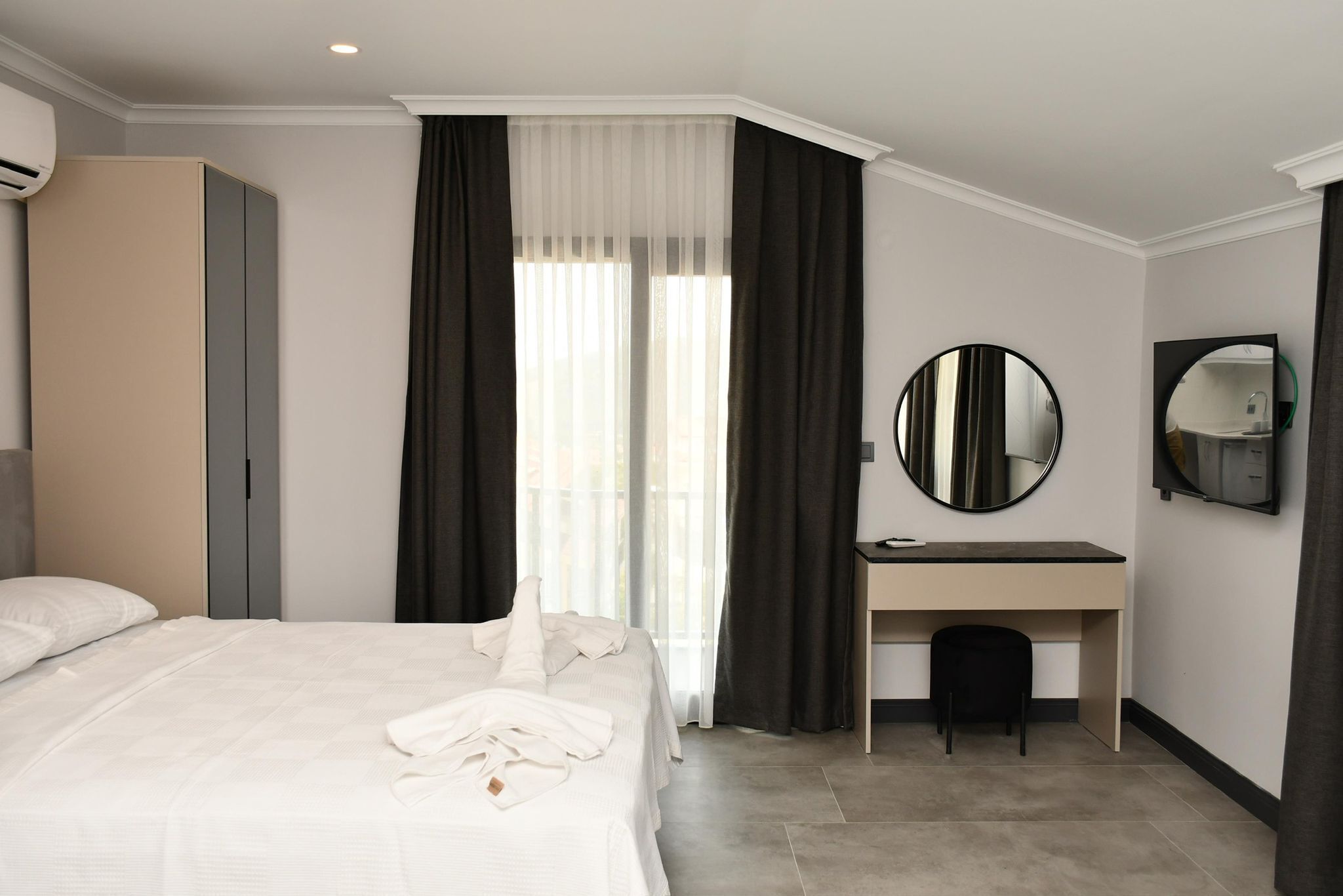 Una habitación de hotel con una cama, un escritorio, una silla, un espejo redondo y un armario.