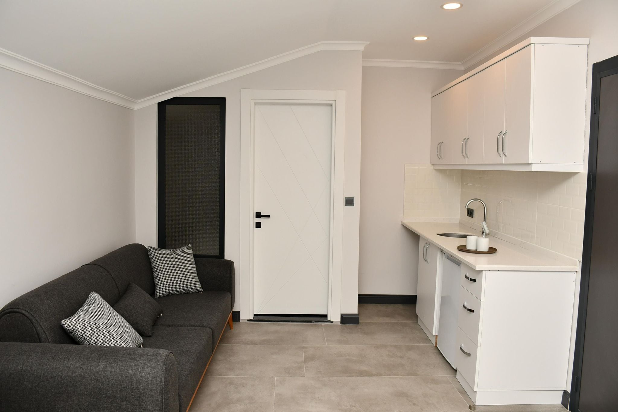 A compact living space with a sofa, a closed door, and a kitchenette.
